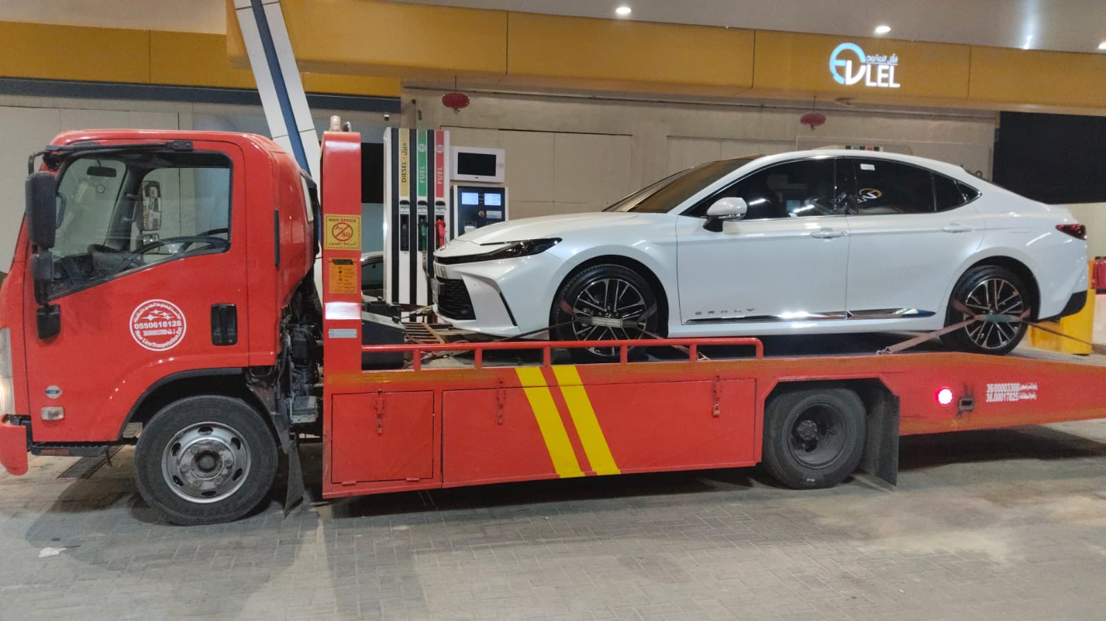 سطحة حمراء تنقل سيارة كامري في محطة وقود في الأحساء